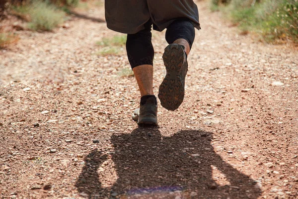 Athletes runner running down a mountain trail. A man runs through the mountains between the stones. View from behind. Man in shorts and black spandex leggings training outdoors.