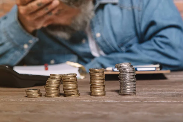 Man at desk in denim shirt holding head and worrying about money.