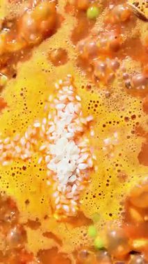 Pirinç, sebze ve et suyu büyük bir tavada kaynarken, şef pirinç ekleyip karıştırıyor.