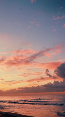 Hafif dalgalar canlı pembe ve mavi gündoğumu gökyüzünün altında kıyıya vuruyor.