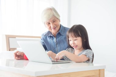 Büyükannesi ile dizüstü bilgisayarda oyun oynayan küçük Asyalı kız