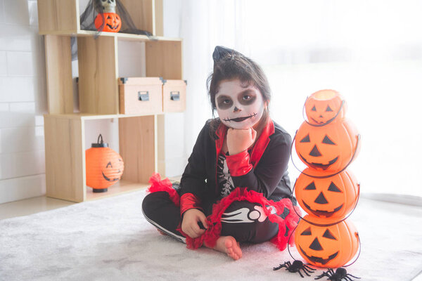 Little asian girl sitting and smile in room decorated for Halloween day