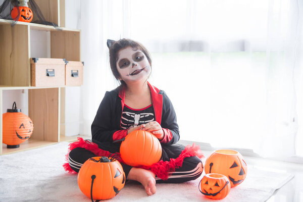 Little asian girl sitting and smile in room decorated for Halloween day