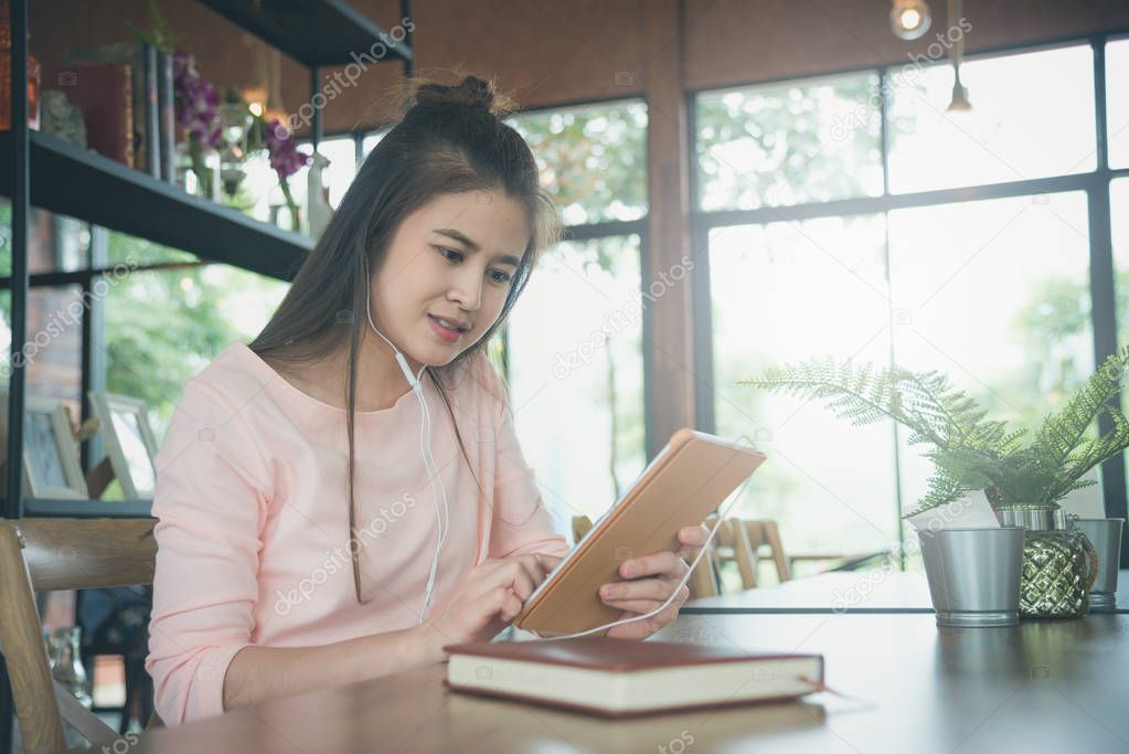 Beautiful asian woman wearing headphones and reading news from tablet computer in coffee shop