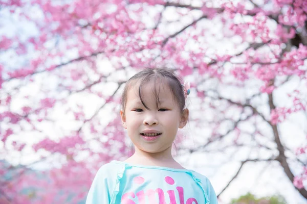 Kleines asiatisches Mädchen lächelt vor einem Sakura-Baum. — Stockfoto