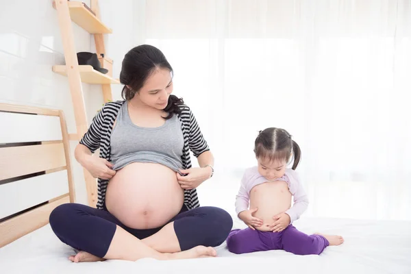 Asya hamile ve kızı yatağa onların göbek gösterilen — Stok fotoğraf