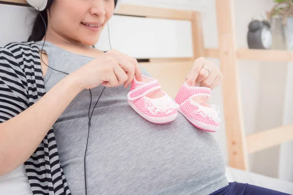 孕妇在肚子上拿着粉红色的婴儿鞋的特写镜头 — 图库照片