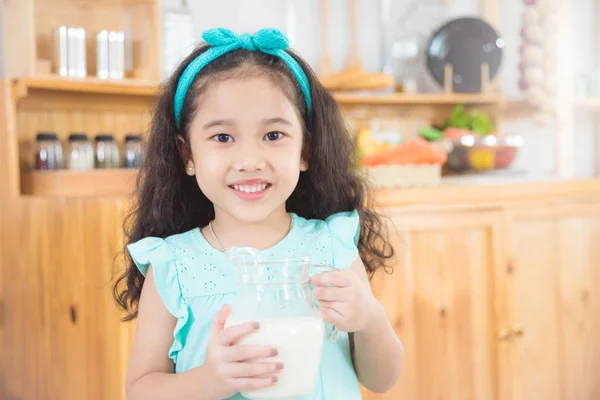 Piccola ragazza asiatica con una brocca di latte e sorrisi — Foto Stock