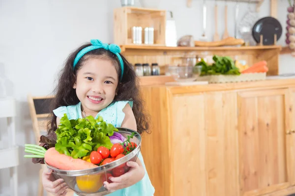 Little asian girl holding basket with many vegetables and smiles — Stock Photo, Image