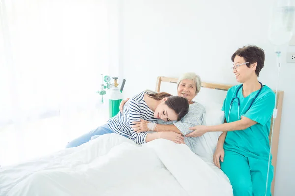 Doctor sitting with happy elderly female patient lying in bed with family