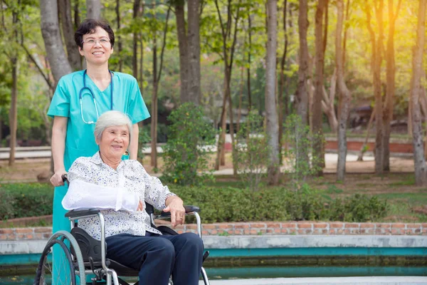 Feliz asiático senior mujer en silla de ruedas con enfermera en jardín —  Fotos de Stock