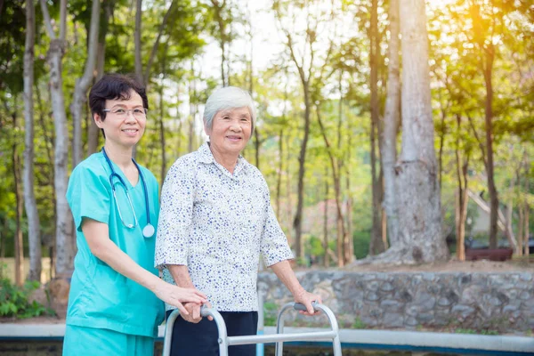 Discapacitados senior asiático mujer caminando con asistencia de enfermera en parque —  Fotos de Stock