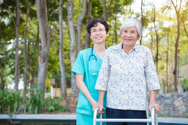 Disabled senior asian woman walking with assistance from nurse in park