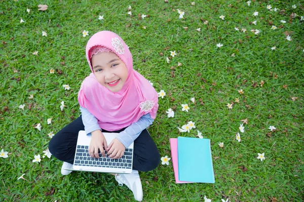 漂亮的穆斯林女孩坐在草地上, 使用笔记本电脑 — 图库照片