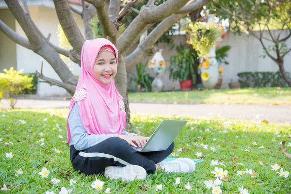 Μουσουλμανικές κορίτσι κάθεται στο γρασίδι και να χρησιμοποιούν φορητό υπολογιστή — Φωτογραφία Αρχείου
