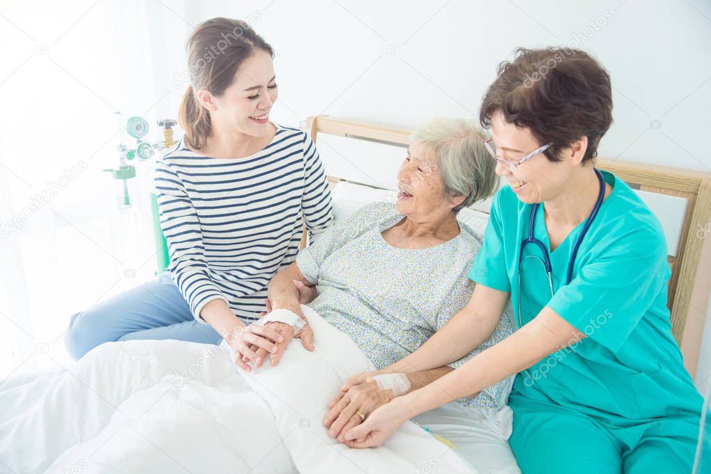 Doctor talking to happy elderly female patient lying in bed with family