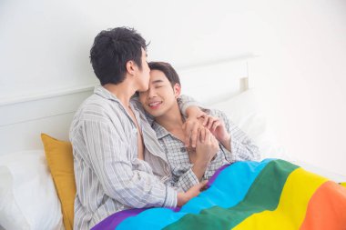 Genç eşcinsel çift, pijama giyip yatakta birlikte yatıyorlar.