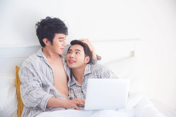 Jong gay paar dragen pyjama liggend op het bed en met behulp van notebook computer — Stockfoto