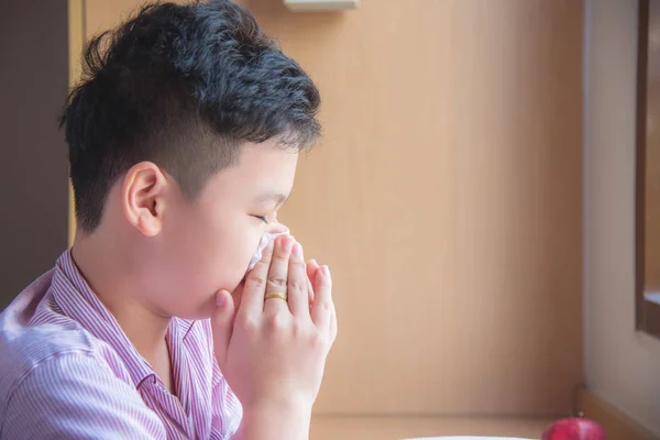 Sick asian boy blowing nose into tissue