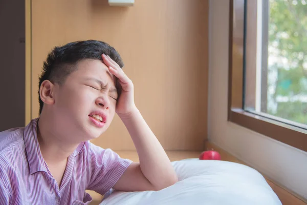 Ung pojke sitter nära fönstret med huvudvärk — Stockfoto