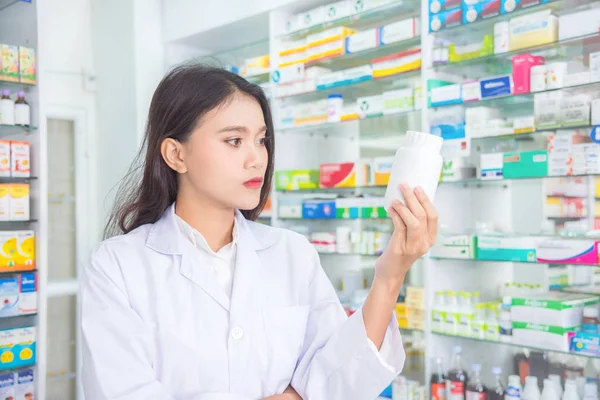 Piękny farmaceuta gospodarstwa i patrząc na butelkę leku — Zdjęcie stockowe