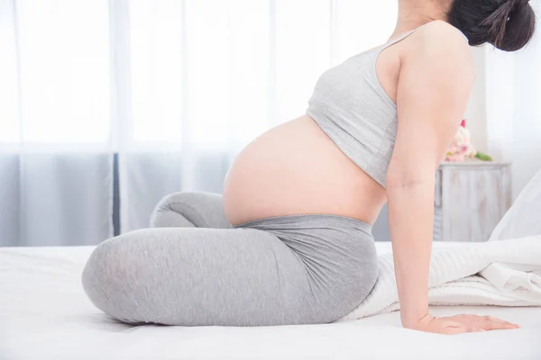 Gravid kvinna sitter på sängen och gör yoga för motion. — Stockfoto