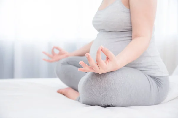Pregnant woman sitting on bed and doing yoga meditation. — Stock Photo, Image