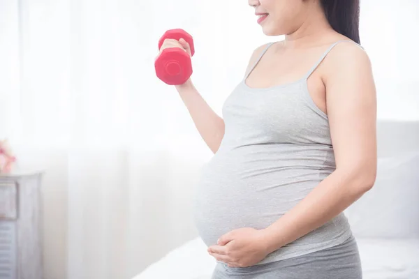 Gravid kvinna stående och hålla bumbell för hand för motion — Stockfoto