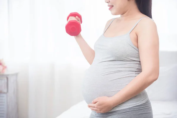 Mujer embarazada de pie y sosteniendo bumbell a mano para el ejercicio — Foto de Stock