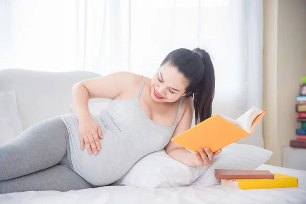 Hermosa mujer embarazada asiática acostada en la cama y tocando su vientre y sonriendo . —  Fotos de Stock