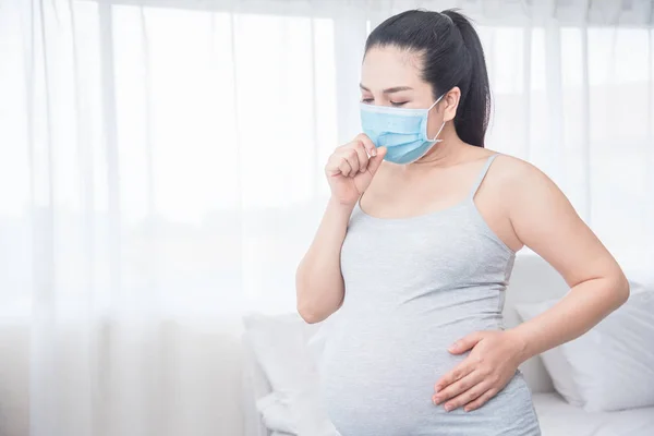 Donna incinta che indossa maschera e tosse nella sua camera da letto . — Foto Stock