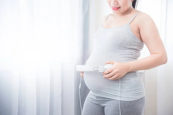 Donna incinta vicino alla finestra e mettere le cuffie sulla pancia — Foto Stock