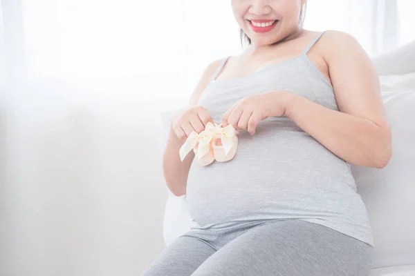 Zwangere vrouw zittend op bed en zet kleine baby slofjes op haar buik Rechtenvrije Stockfoto's
