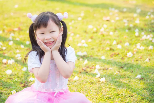 สาวน้อยนั่งและยิ้มบนสนามหญ้า — ภาพถ่ายสต็อก