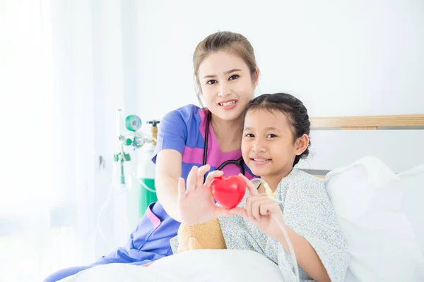 Lány beteg és női orvos gazdaság vörös szív labdát, és mosolyog — Stock Fotó