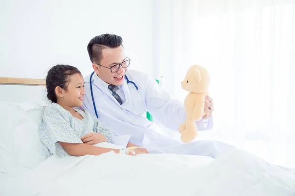 Pediatra varón médico sosteniendo osito de peluche y jugando con niño paciente — Foto de Stock