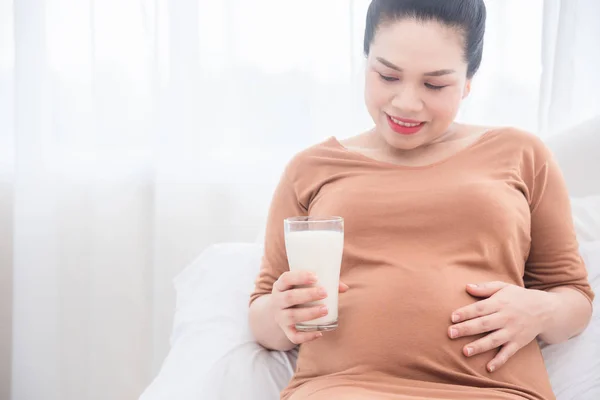 孕妇坐在床上，拿着一杯牛奶和微笑 — 图库照片