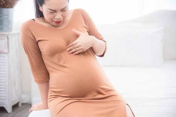 Schwangere Asiatin sitzt auf Bett und leidet an Herzverbrennungen — Stockfoto