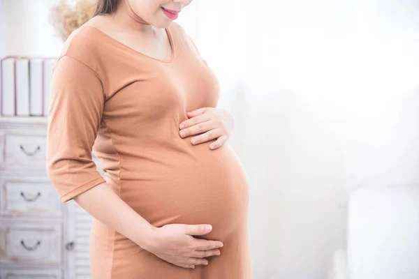 Hamile kadın ayakta ve gülümseyen karnına el ele tutuşuyor — Stok fotoğraf