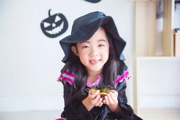 Klein meisje in Halloween heks kostuum zittend en houden van chocolade — Stockfoto