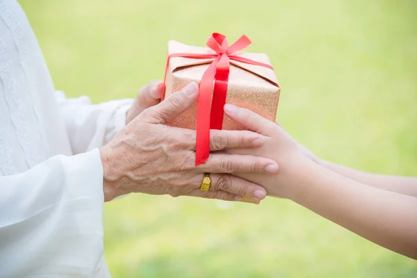 Closeup on young girl hands giving gift box to elderly woman — Stock Photo, Image