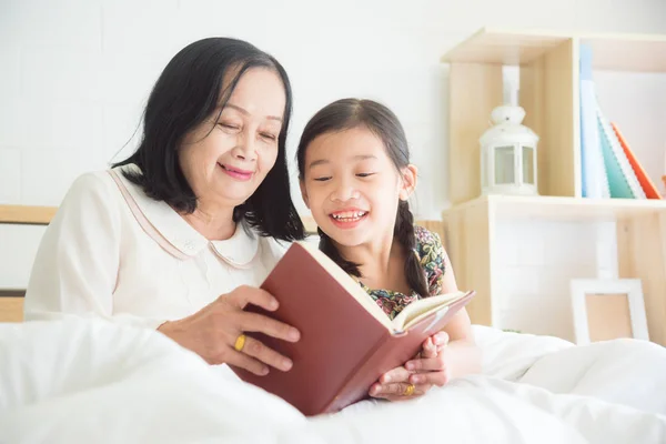 Senior vrouw lezen boek met kleindochter op bed. — Stockfoto