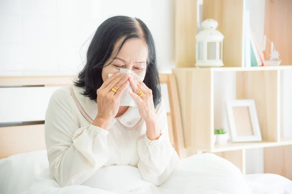 Wanita senior yang tidak sehat meniup hidung di tempat tidur, wanita senior yang menutupi hidung dengan kertas tisu — Stok Foto