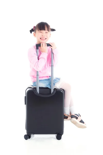 Kleine Aziatische meisje zittend op wiel koffer en glimlacht — Stockfoto