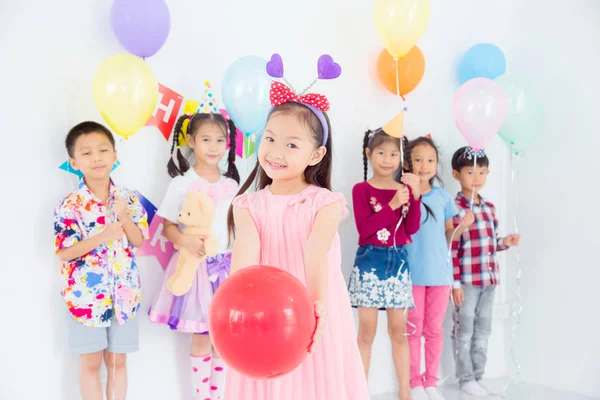Μικρό όμορφο κορίτσι κρατώντας κόκκινο μπαλόνι και χαμόγελα στο πάρτι γενεθλίων — Φωτογραφία Αρχείου