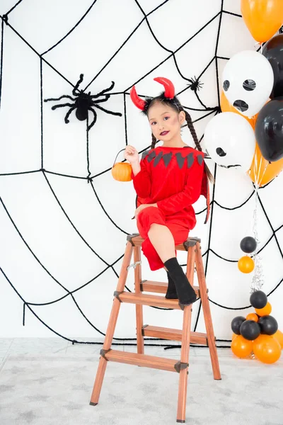 Mooi meisje in rode duivel kostuum met hoorn zittend in de kamer — Stockfoto