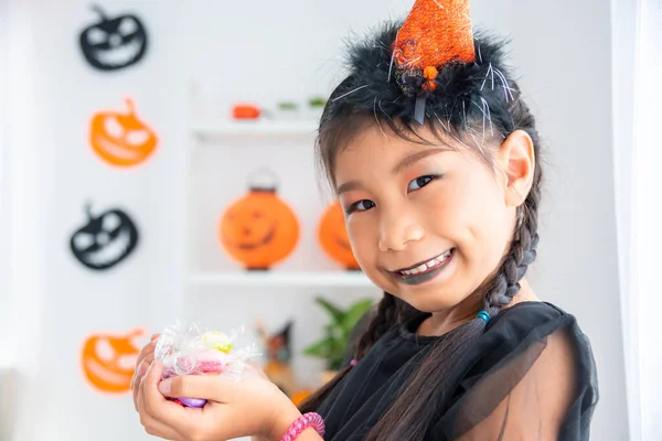 Kis Ázsiai Lány Boszorkányruhában Mosolyog Sok Cukorkát Tart Kezén Halloweenkor — Stock Fotó