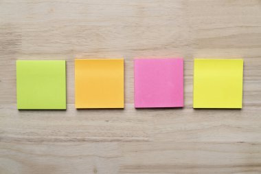 Ahşap masa arka plan üzerine yapıştırılmış yeşil, turuncu, pembe ve sarı yapışkan not kümesi