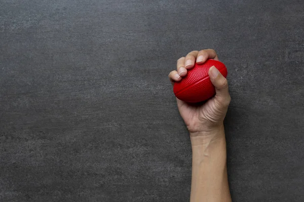 Manos de una mujer apretando una bola roja de estrés en la mesa de madera — Foto de Stock