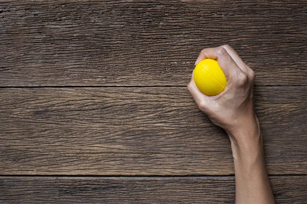 Hands of a woman squeezing a yellow stress ball on the wooden ta